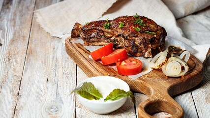 Grilled steak on a cutting board. Appetizing roasted meat with vegetables and herbs. Copy space. Rustic wooden table background.
