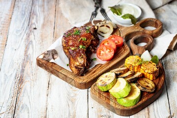 Grilled steak on a cutting board and assorted grilled vegetables. Appetizing grilled meat with vegetables and herbs, sauce. Copy space. Rustic wooden table background.