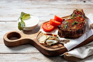 Grilled steak on a cutting board. Appetizing roasted meat with vegetables and herbs. Copy space. Close-up