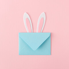 Flat lay composition made with bunny rabbit ears and paper envelope on pastel pink background. Happy Easter minimal concept.