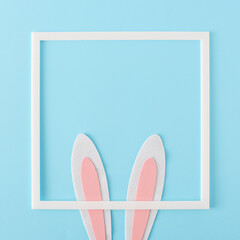 Happy Easter minimal concept. Bunny rabbit ears and white frame on pastel blue background, flat lay.