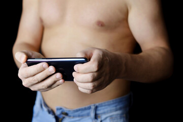 Muscular man in jeans with naked torso with smartphone in hands. Concept of watching video, online communication