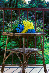 żółto-niebieskie jasne kwiaty na słomianym stole na balkonie z widokiem na ogród w ciepłych promieniach jesiennego słońca