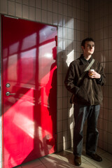 Stockholm, Sweden A young man stands next to a red door with a cup of take-away coffee in a train station.