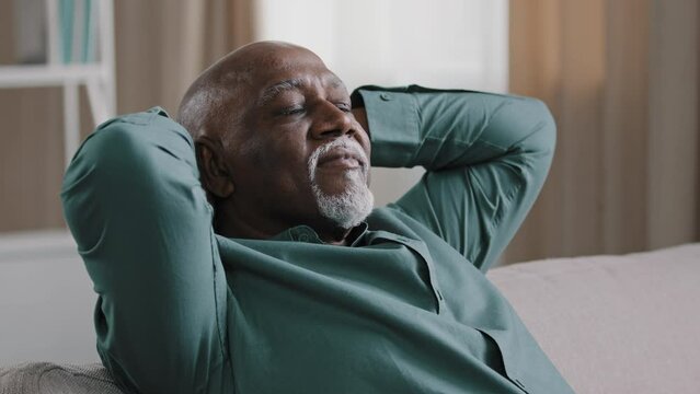 Portrait of contented elderly african american man smiling happy carefree grandpa resting at home holding hands behind head healthy calm retiree relaxing napping with eyes closed on comfortable sofa
