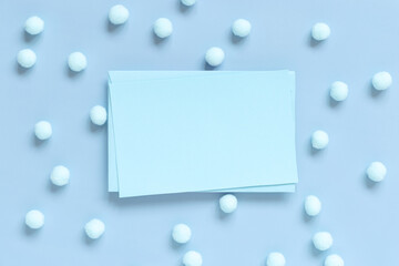 Blank card between pastel pom-poms on light blue top view