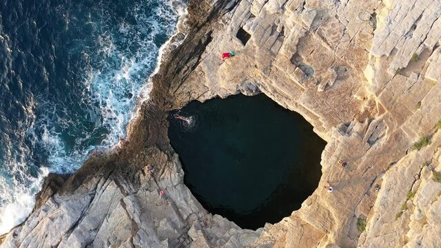 Flying above a woman swimming in a natural sea pool on rocky coastline. Giola lagoon, Thassos island, Greece, aerial drone view