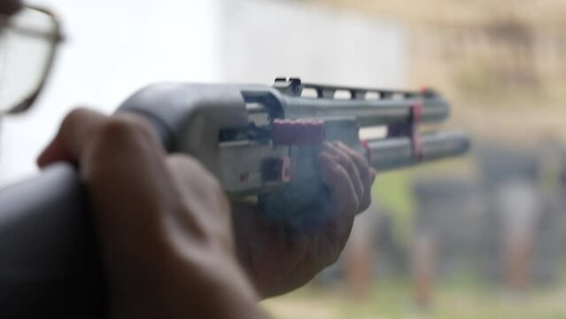 Man shoots with a combat shotgun at targets on the shooting range, close up, slow motion. Back view of man shooting shotgun at target while practicing