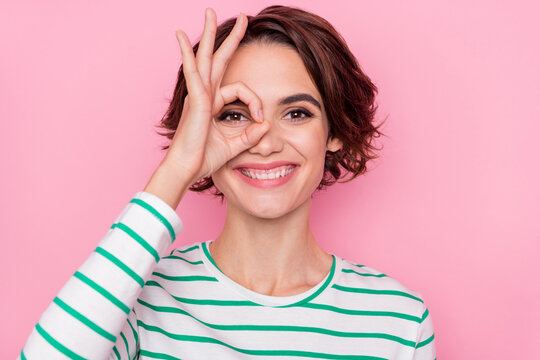 Portrait of attractive cheerful girl showing ok-sign like watch look see isolated over pink pastel color background