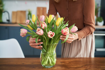 Caucasian woman putting fresh tulips into the vase - obrazy, fototapety, plakaty