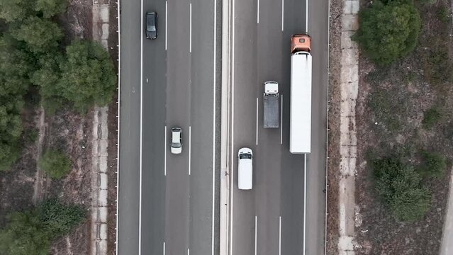A vertical shot made above the highway. Vehicles drive in both directions. Accidental trees grow on both sides of the road.
