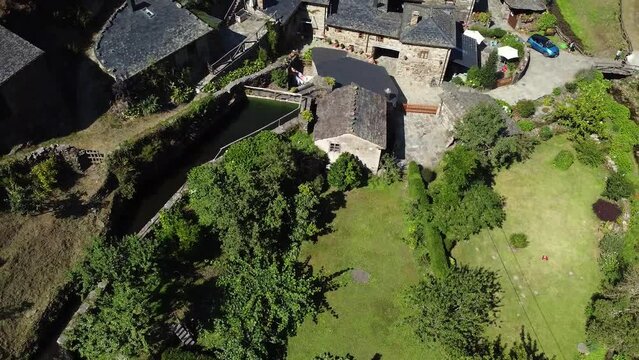 Aerial shot, drone flying backward from a little town (backward) on the valley of the green mountains of Asturias, Spain. Thic forest covering mountain surface under a clear blue sky in pure daylight.