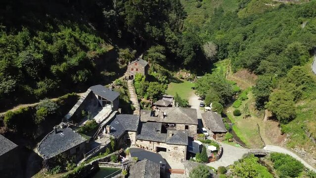 Aerial shot, drone flying over a little town (backward) on the valley of the green mountains of Asturias, Spain. Thic forest covering mountain surface under a clear blue sky in pure daylight.