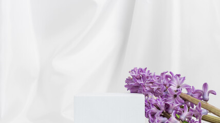 White cube empty podium with spring hyacinth flowers on white textile drape background. Podium to display products, perfume and cosmetics