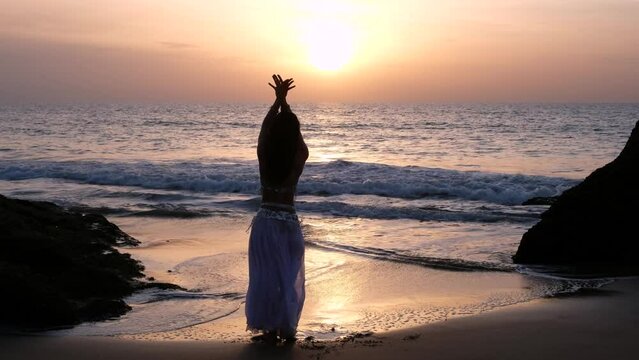 A beautiful woman performing a sensual belly dance in the sand on the beach. Spectacular landscape with blank holes. Silhouette.