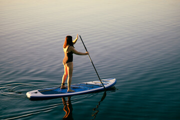 View from above on relaxed middle aged woman on sup board rowing with oar on calm lake water....
