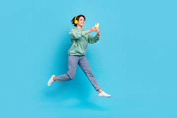 Fototapeta premium Full length photo of funky millennial brunette lady run look telephone wear headphones pullover jeans shoes isolated on blue background