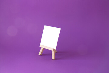 Wooden easel with a blank white sheet of paper on a bright purple background