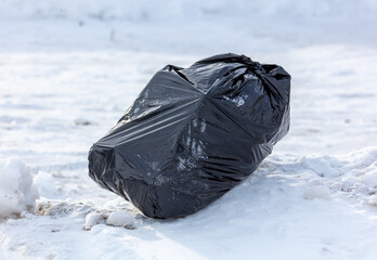 Black bag with garbage on the snow