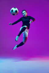 Fototapeta na wymiar One sportive girl, female soccer player kick in jump football ball isolated on purple studio background in neon light. Sport, action, motion, fitness