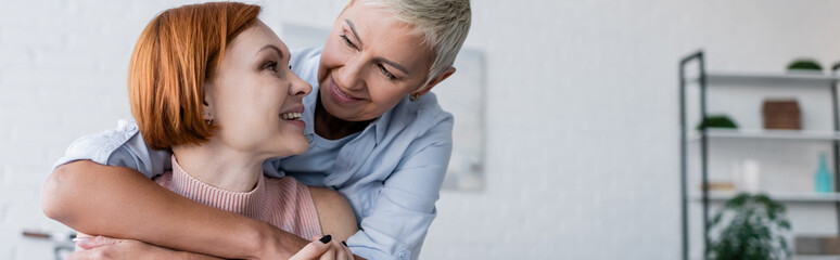 smiling lesbian women looking at each other at home, banner