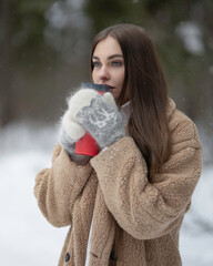 Girl with a red thermal mug in the winter forest