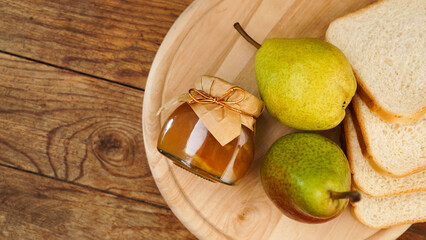 Jar of tasty pear jam with bread and fresh pear fruit on wooden table. Top view. Homemade marmalade, confiture in a glass jar