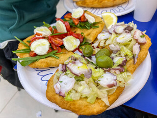 Pizze fritte aperte con sopra, polipo, insalata, olive, mozzarella di bufala, rucola e pomodori freschi