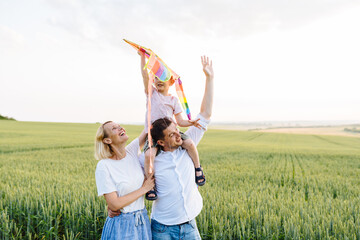 Mother, father and child having fun try to fly with kite field on summer sunset, outdoor. Portrait...