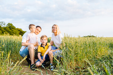 Naklejka na ściany i meble Parents and two sons relationship. Mom and dad hugs their kids. Walking on a beautiful fiels. Children and parents holding hands. Freedom and love concept. Happy family in a nature.