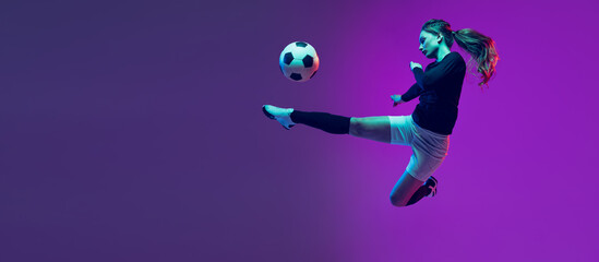 Emotive girl, female soccer, football player in motion, action isolated on purple studio background...