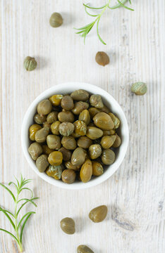 Pickled capers on white wooden surface. Gourmet food.