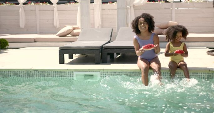 Two little girls sitting at poolside and eating watermelon