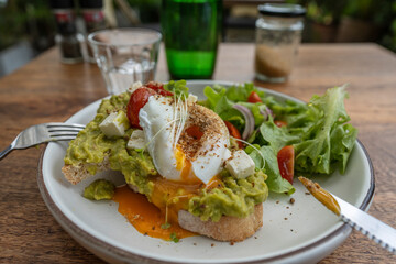 Sourdough toast, poached eggs, avocado pulp and fresh vegetables on plate in cafe, close up