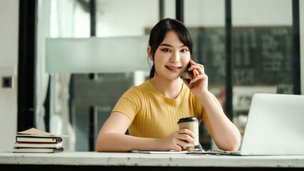 Attentive asian woman sit at desk and call the phone at coffee cafe.