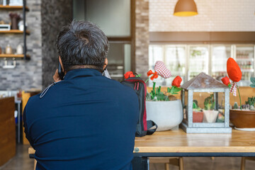 Back view of busy mature businessman calling his wife in cafe on Valentines day with red heart ornaments and rose blurred in background.Selective focus on mobile phone.Love and Valentines day concept
