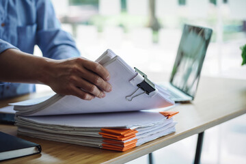 Asian male office worker holding documents of unfinished paperwork on office table.