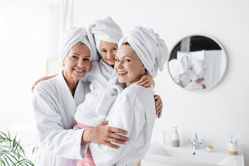 Positive lesbian mothers holding kid in bathrobe in bathroom