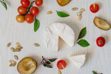 Charcuterie board of assorted cheeses, vegetables and appetizers. Above Top view table scene on a white wood background.