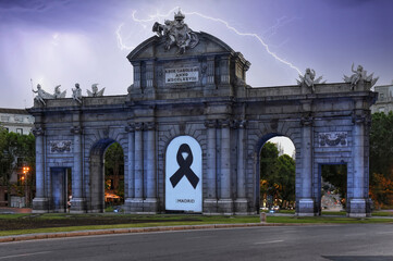 Obraz premium Vista de la Puerta de Alcalá en Madrid con su arco central tapado con un cartel recordando a los muertos por Covid bajo un cielo iluminado por relámpagos