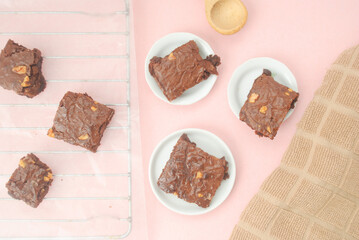 Baked brownies on a metal grid and a white plates, a kitchen towel on a pink background 