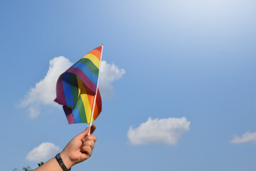 Pride rainbow lgbt gay flags holding in hand and being waved in the breeze against blue sky.