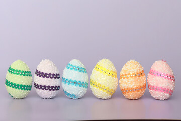 Green, purple, blue, yellow, orange, yellow eggs in a row on a purple background. Geometry. Minimal concept. Easter card with a copy of the place for the text.