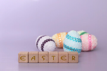 Colorful decorative eggs for Easter holiday, inscription on wooden Easter cubes, purple background