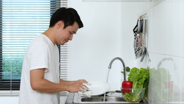Happy young man washing dishes in the sink in the kitchen at home