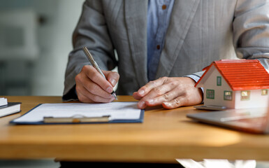 Close up house model mortgage loan with businessman real estate broker signs a purchase contract or mortgage for a Home Interiors, real property estate concept.