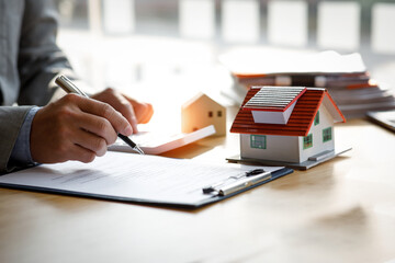Fototapeta premium Close up house model mortgage loan with businessman real estate broker signs a purchase contract or mortgage for a Home Interiors, real property estate concept.