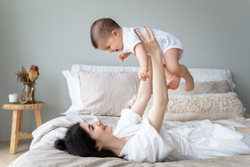 Happy mother holds baby in the air. A young mother is playing on the bed with her child. Happy childhood.