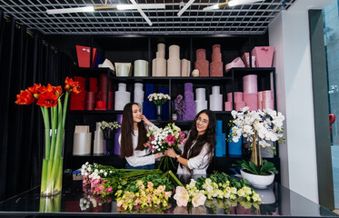 Two young women take orders and make up a beautiful festive bouquet in a cozy flower shop. Floristry and making bouquets in a flower shop. Small business.