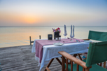 Table set for two on sea coast. Romantic table setting on the sunset. Outdoor restaurant on the beach. Elegant cafe decoration on terrace. Tropical restaurant in summer twilight.